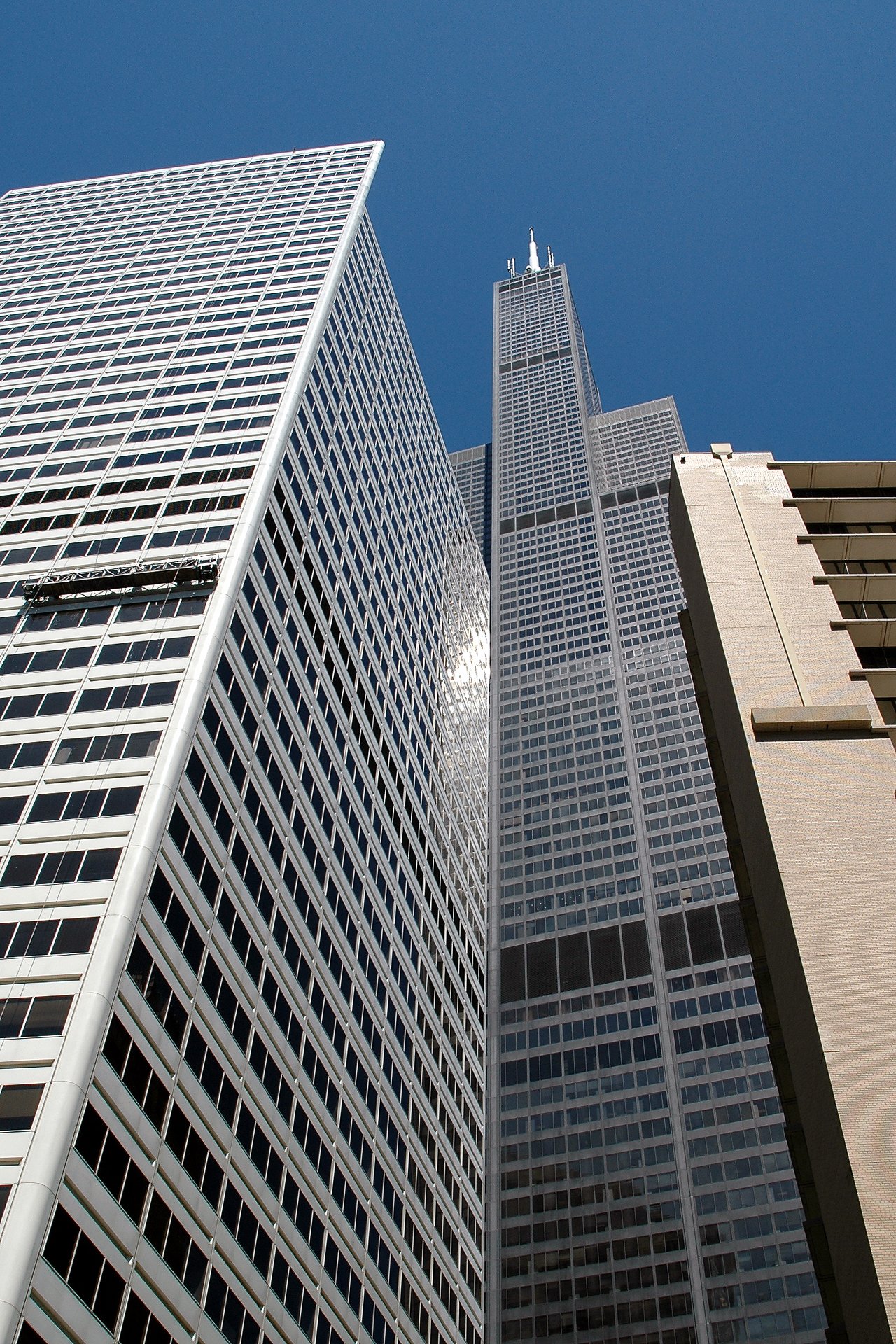 Looking up at the Sears Tower and surrounding skyscrapers against a clear blue sky in Chicago.