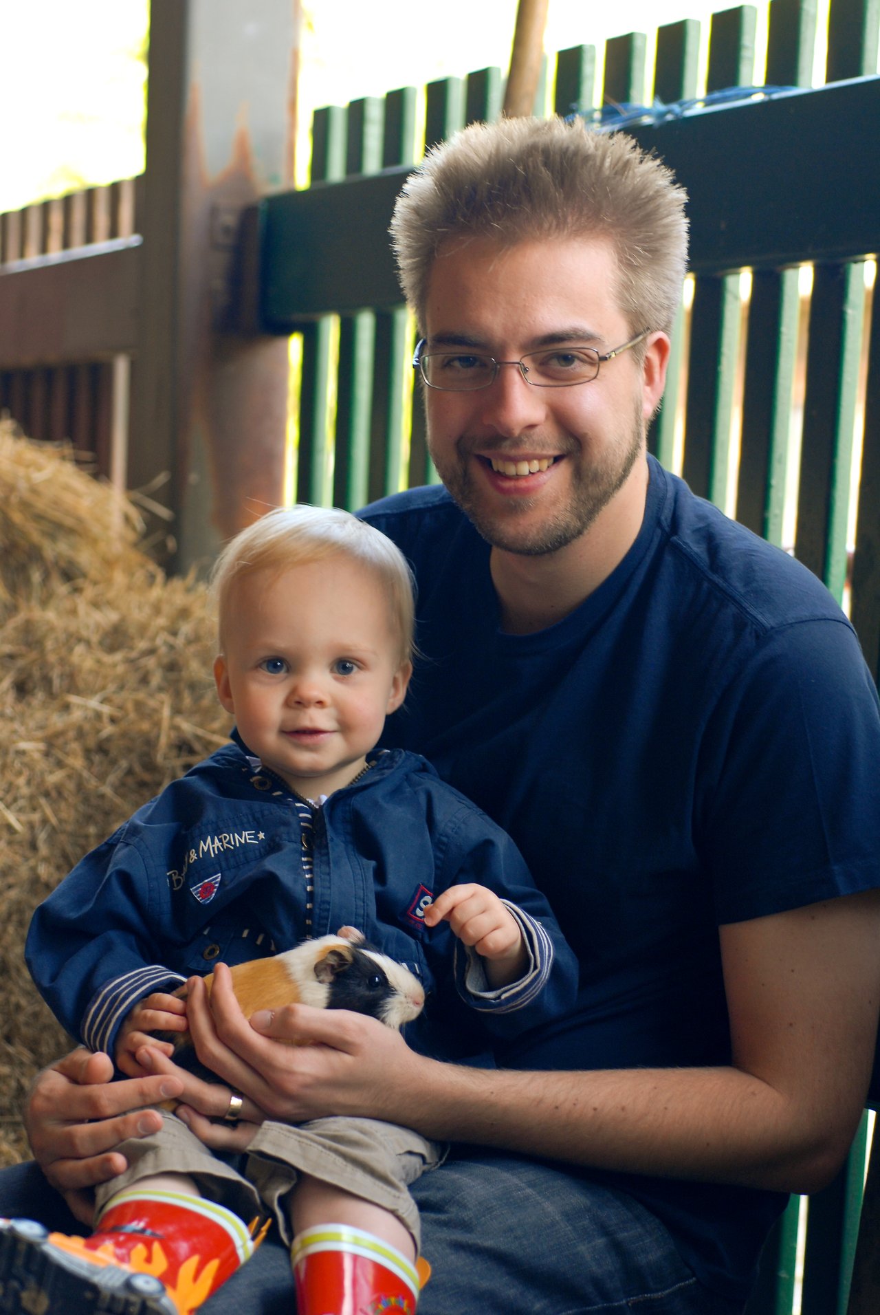 A man and a young child sit together, smiling while holding a small guinea pig in their hands.