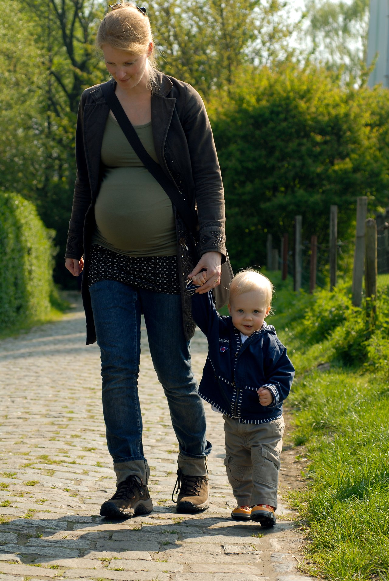 A woman and a young child walk on a cobblestone path, holding hands.