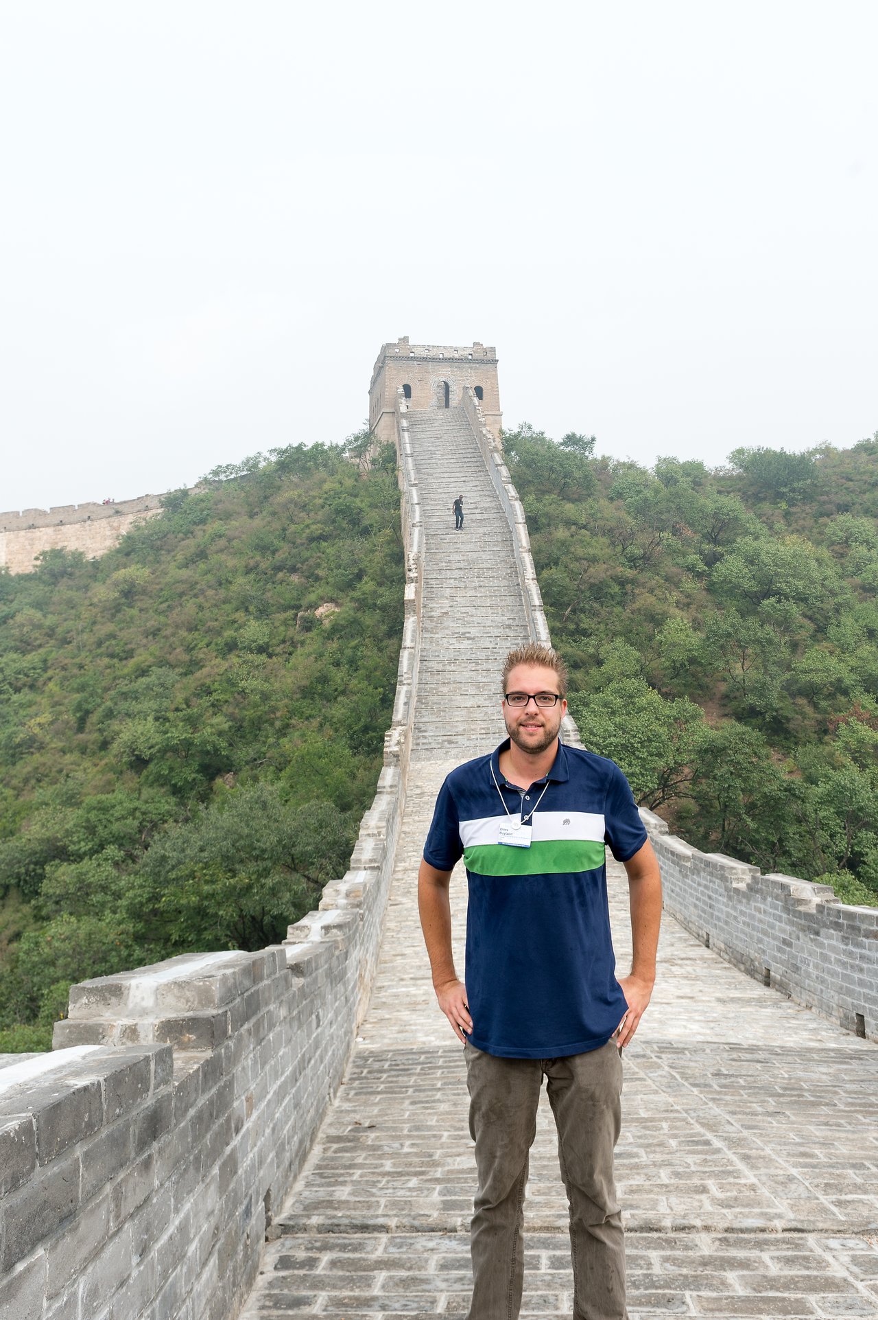 A man stands on the Great Wall of China, smiling at the camera, with a steep staircase behind him.
