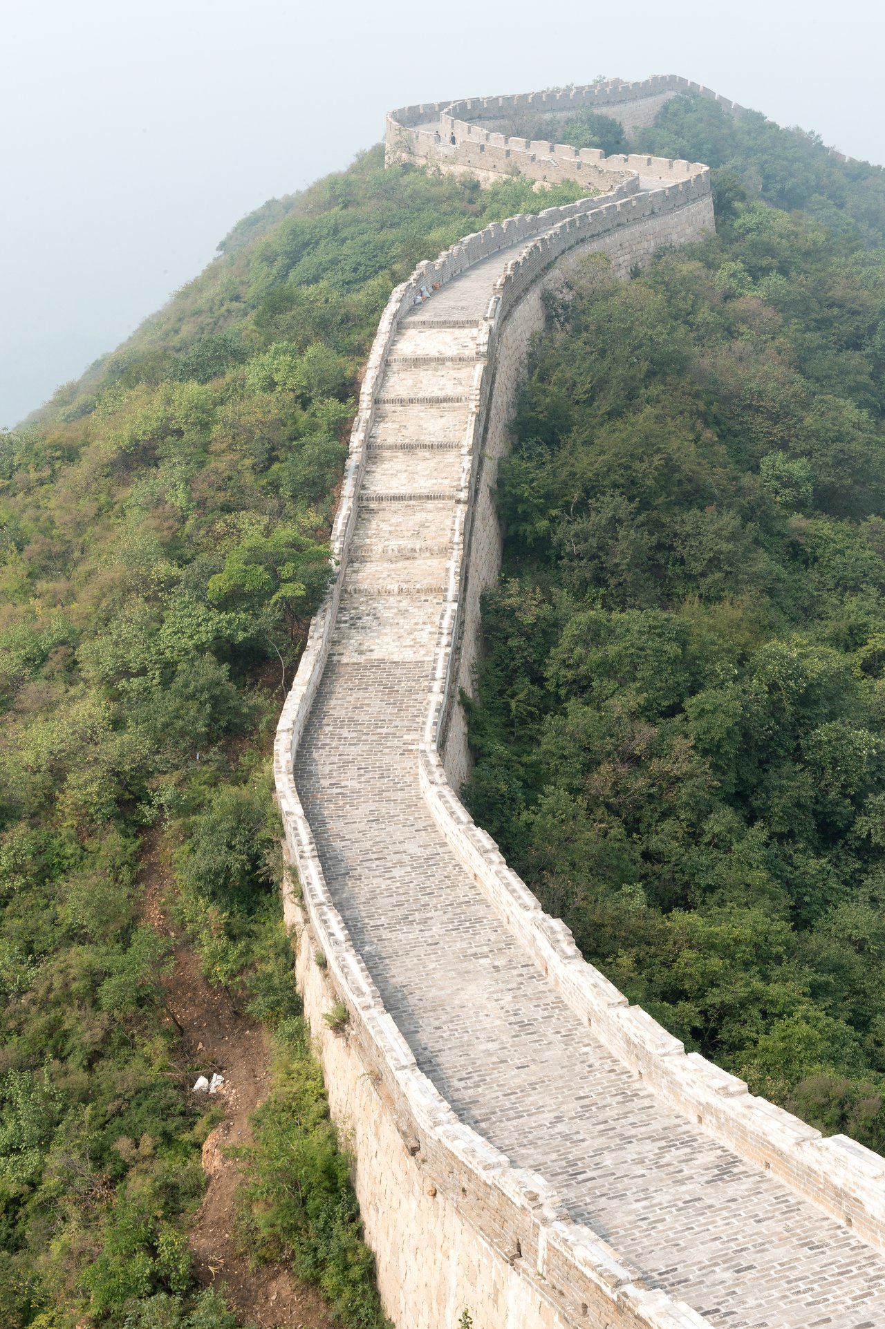 A section of the Great Wall of China curves over a green hillside, with stone steps leading upward.