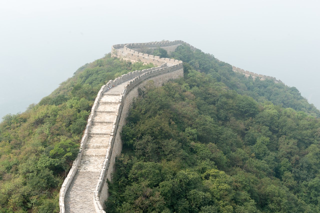A section of the Great Wall of China winding over a green hillside, partially covered in mist.