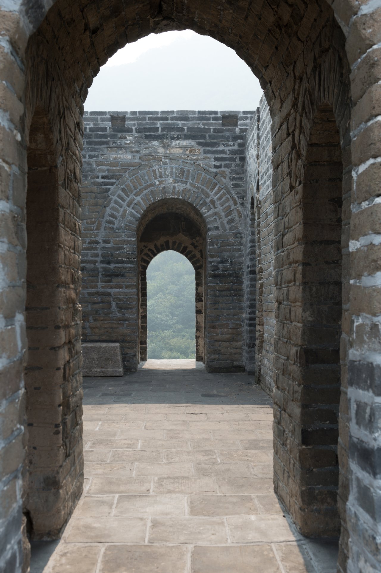 Stone archways along the Great Wall of China, leading to an open view of distant greenery.