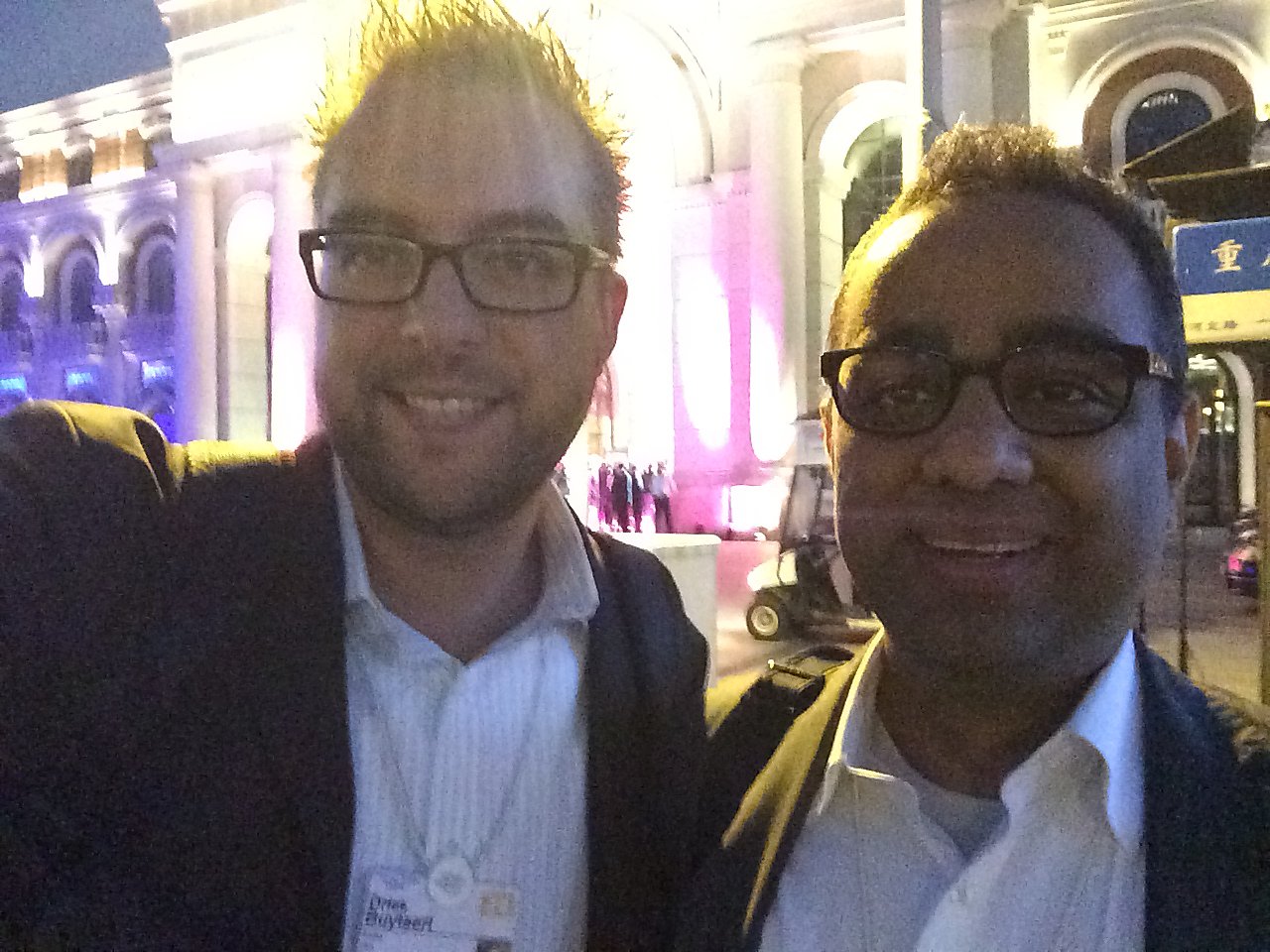 Two men wearing glasses and business attire take a selfie outside a well-lit building at the World Economic Forum.