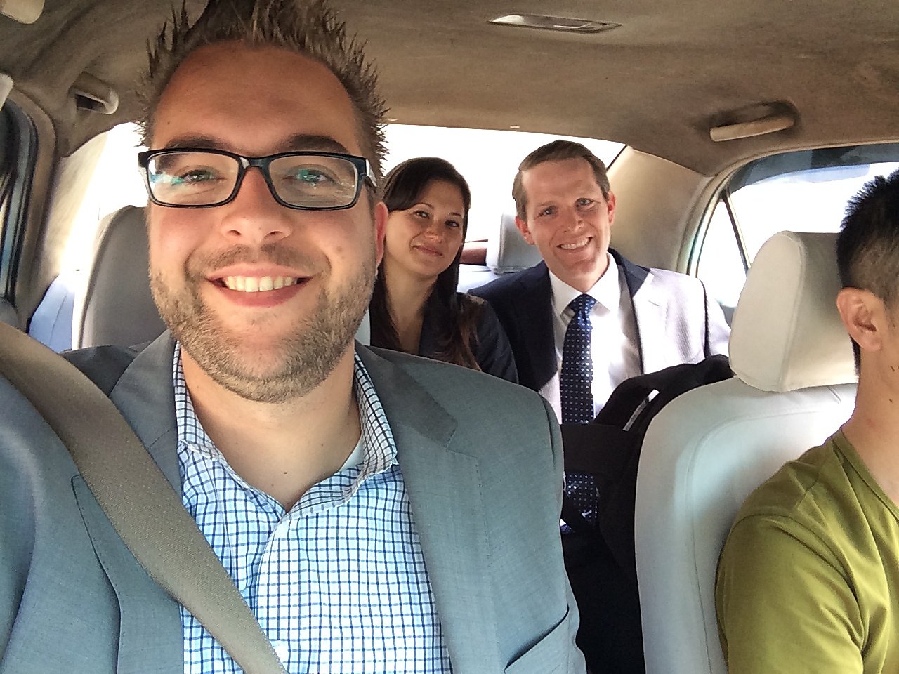 A group of people in business attire smiling inside a car, possibly traveling to the World Economic Forum.