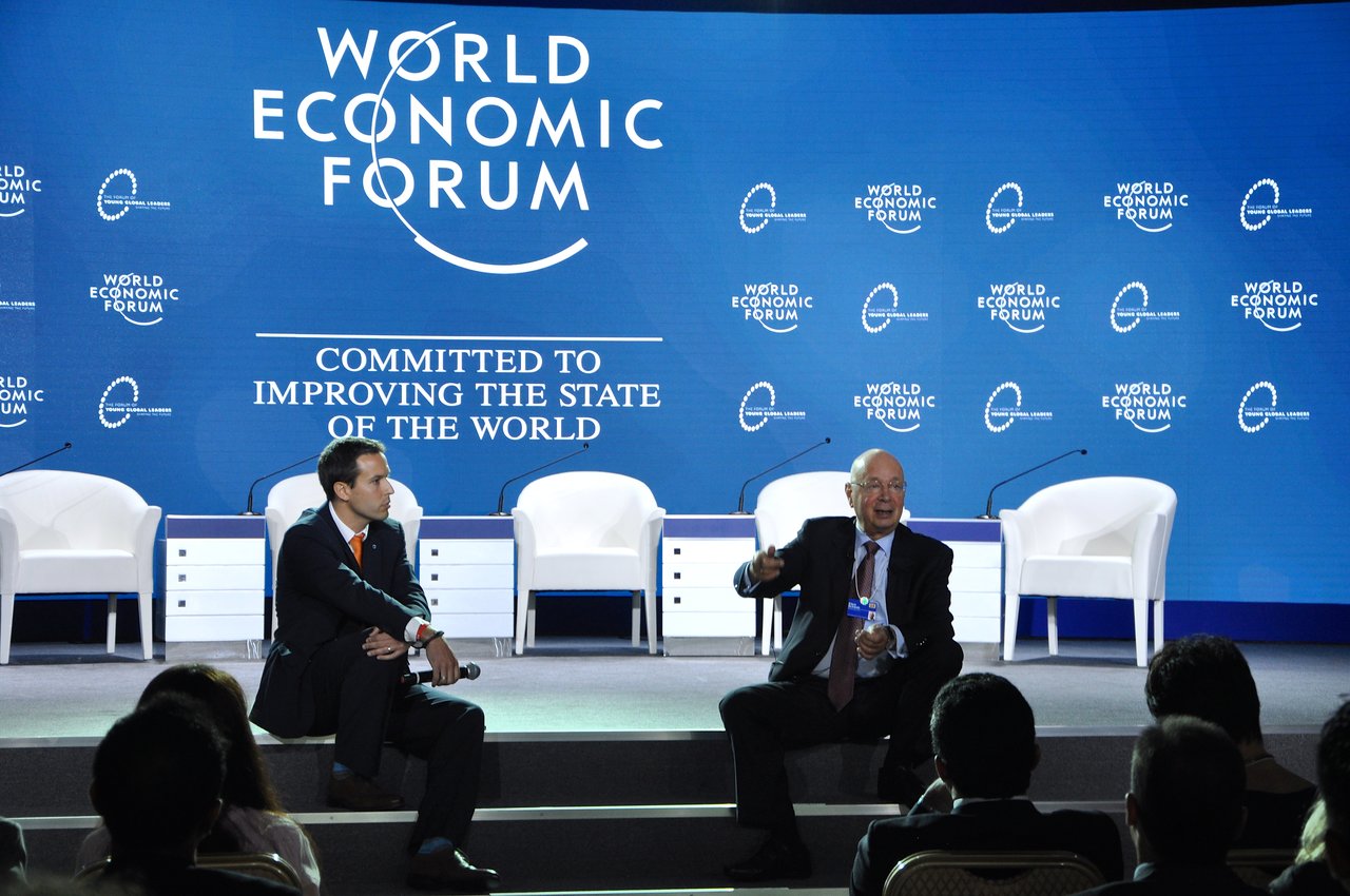 Two speakers discuss on stage at the World Economic Forum, with an audience listening attentively.