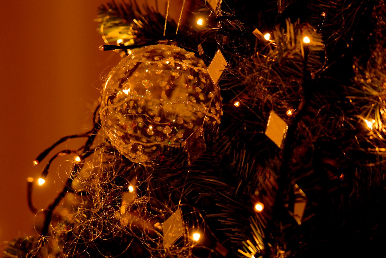 A decorated Christmas tree with glowing lights and a clear ornament hanging among the branches.