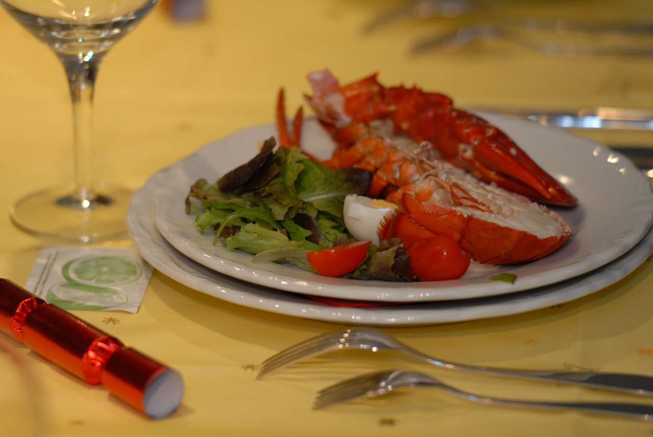 A plated lobster with salad, cherry tomatoes, and a boiled egg on a festive table with utensils and decorations.