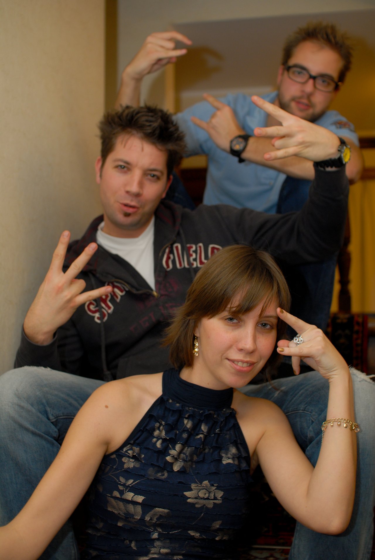 Three people posing playfully indoors, making hand gestures and looking at the camera with relaxed expressions.