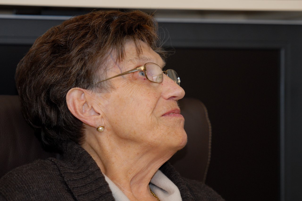Elderly woman with glasses sitting and looking to the side with a calm expression.