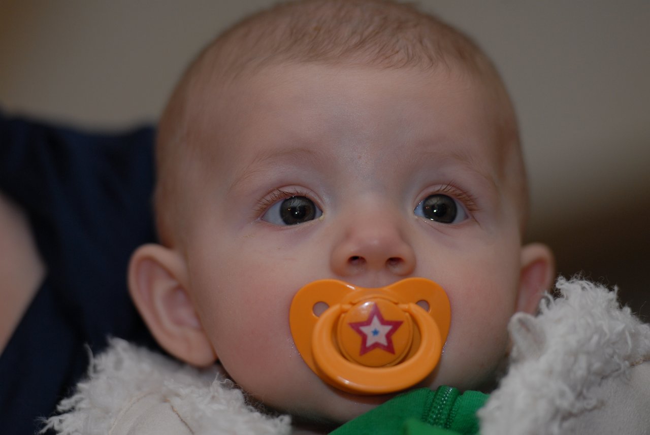 A baby with a pacifier looks ahead, wearing a warm outfit.