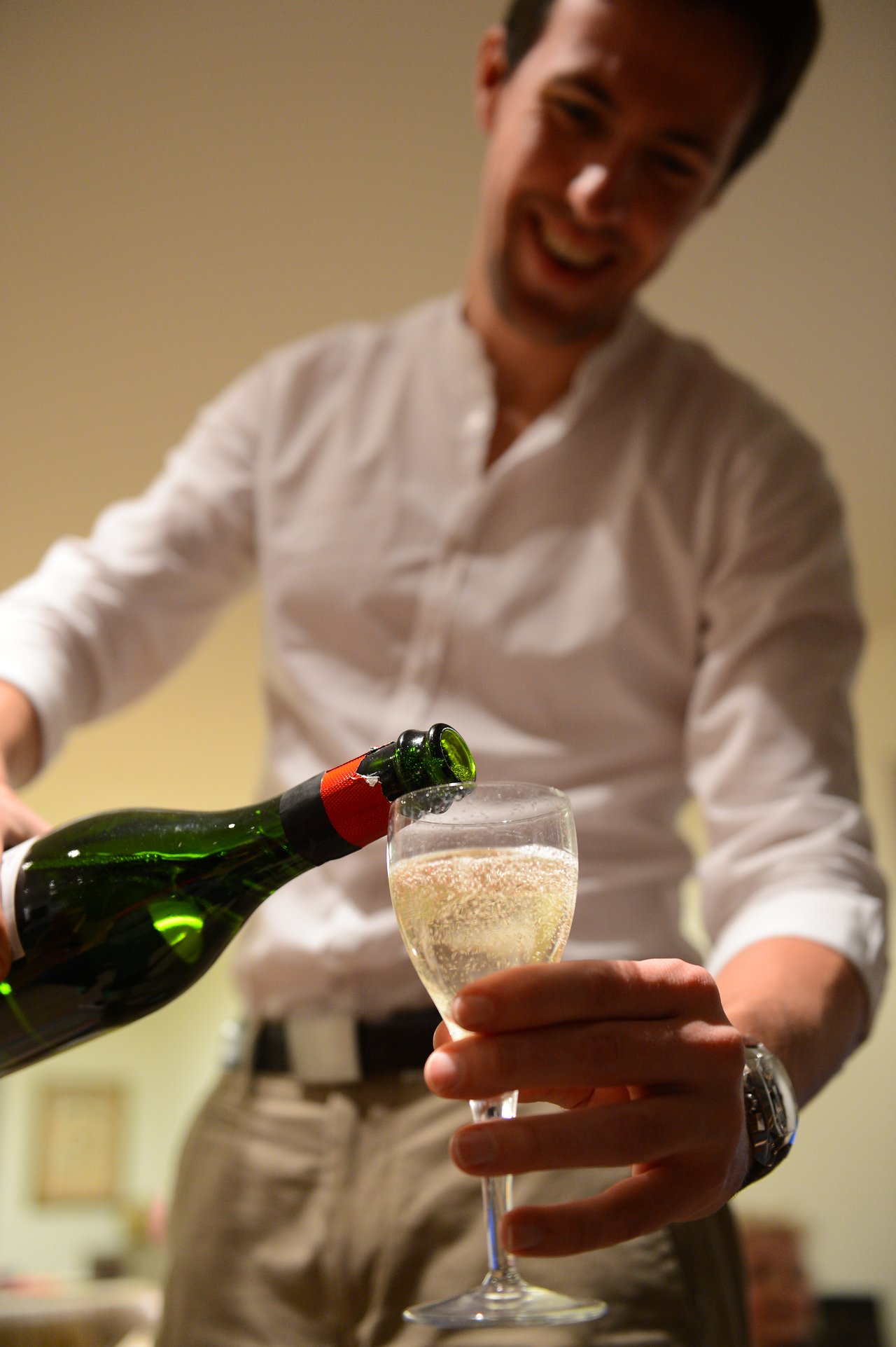 A person in a white shirt pours champagne into a glass, holding it steady with their other hand.
