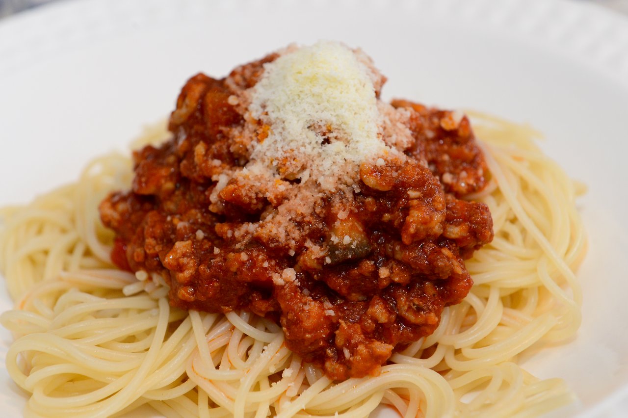 A plate of spaghetti with meat sauce, topped with grated cheese, served on a white dish.