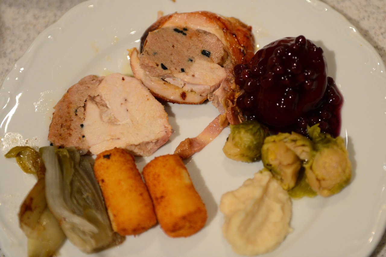 A plate of Christmas dinner with stuffed meat, croquettes, Brussels sprouts, mashed potatoes, and cranberry sauce.