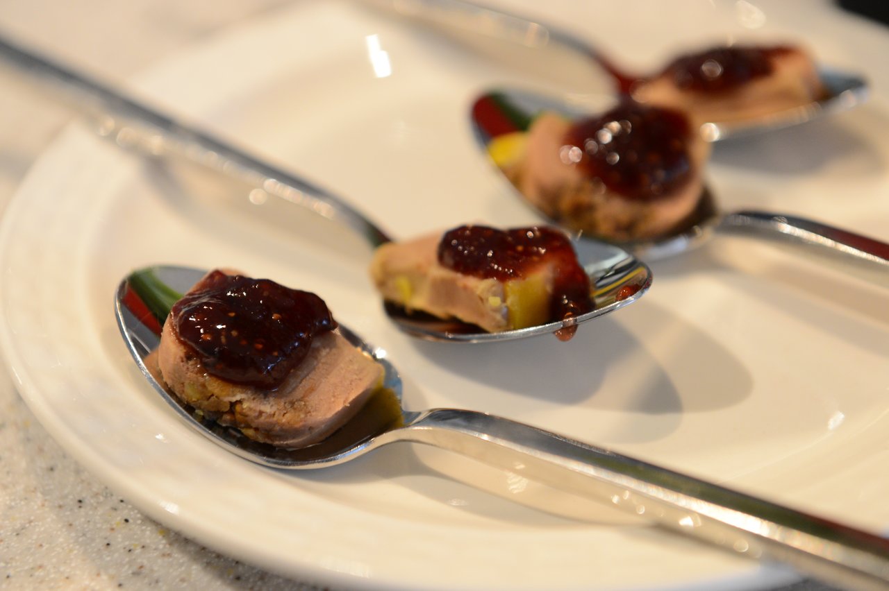 Spoons with small portions of pâté topped with red fruit jam are arranged on a white plate.