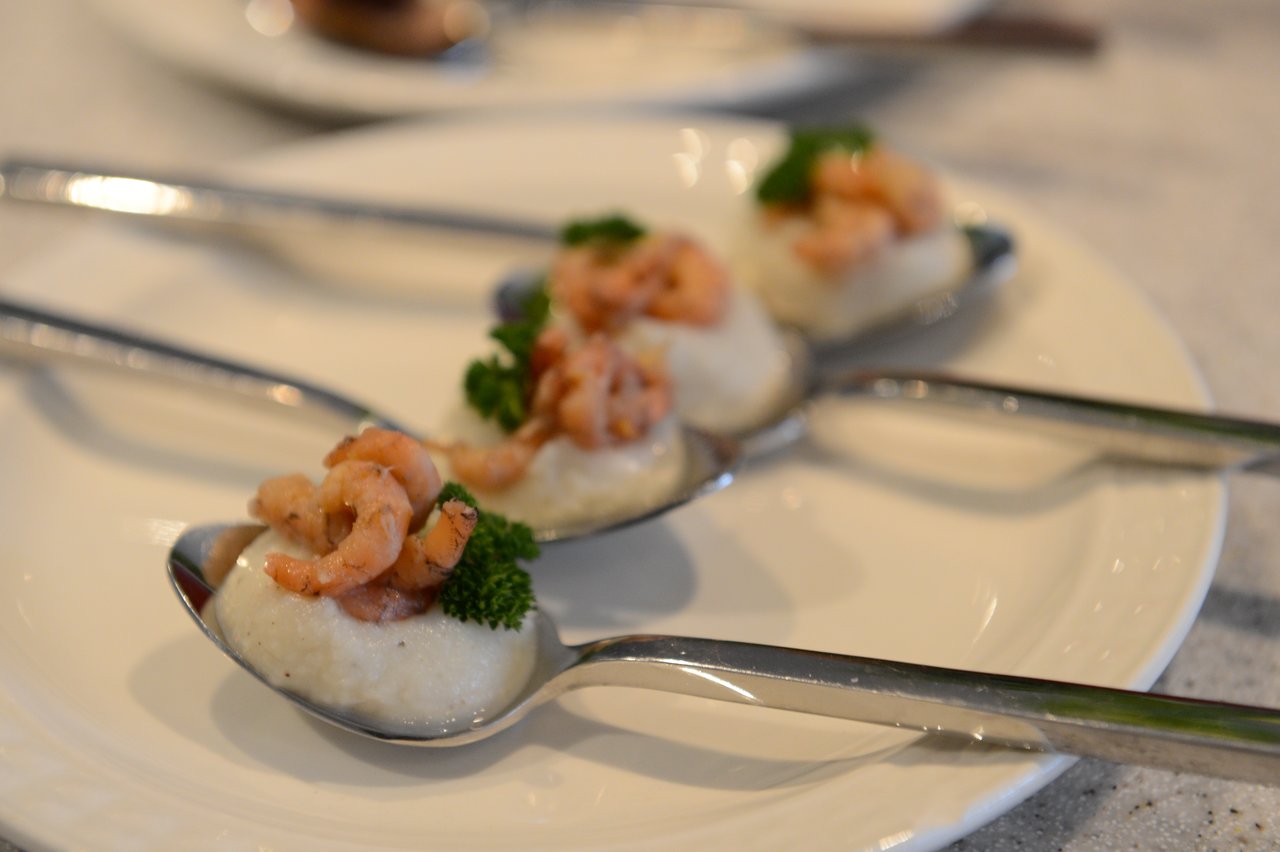 Three spoons with shrimp, creamy sauce, and parsley are arranged on a white plate.