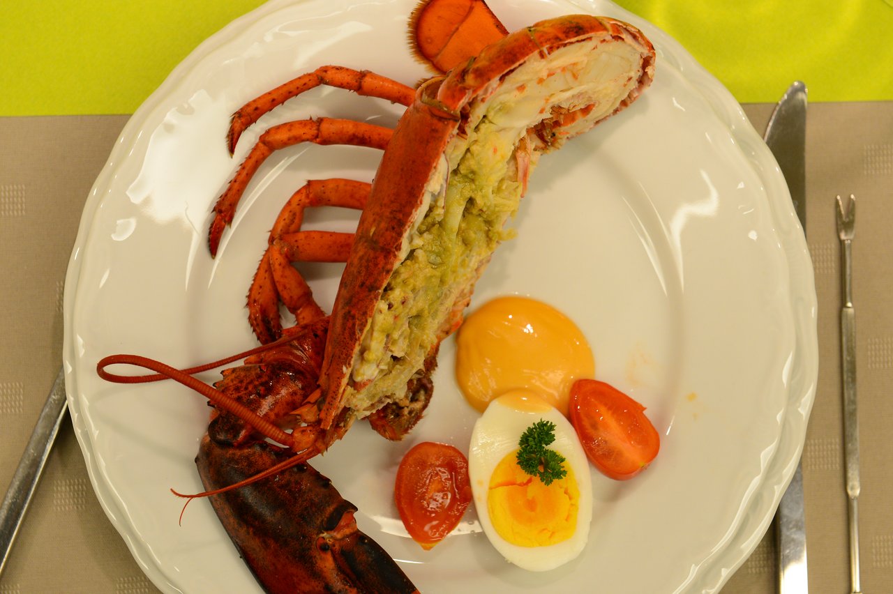 Stuffed lobster served on a white plate with boiled egg, cherry tomatoes, and sauce.