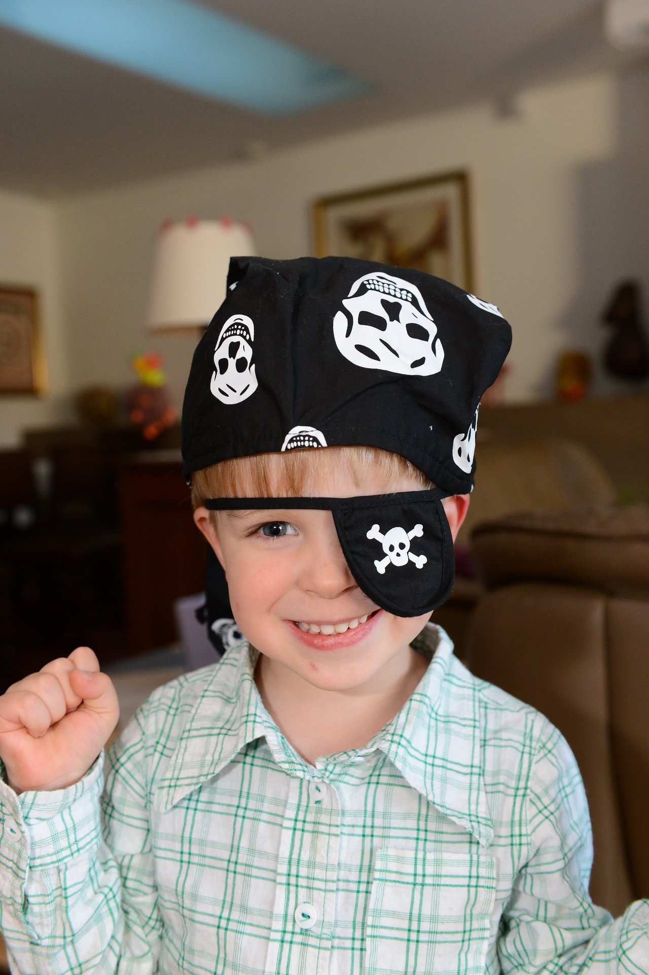 A smiling child wears a pirate bandana and eye patch, raising a fist in a playful pose.