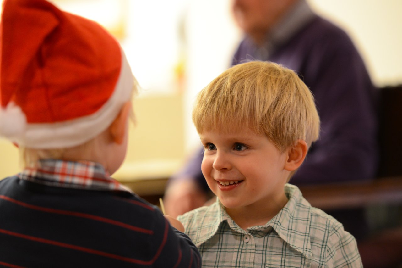 Two young children play together, one wearing a Santa hat, while smiling and interacting in a festive setting.