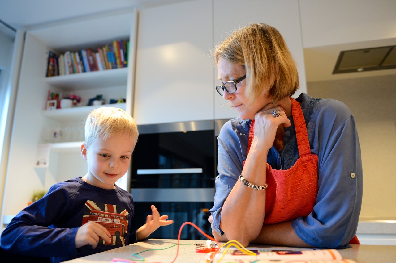 A young boy and an adult work on a simple electrical circuit together at a kitchen counter.