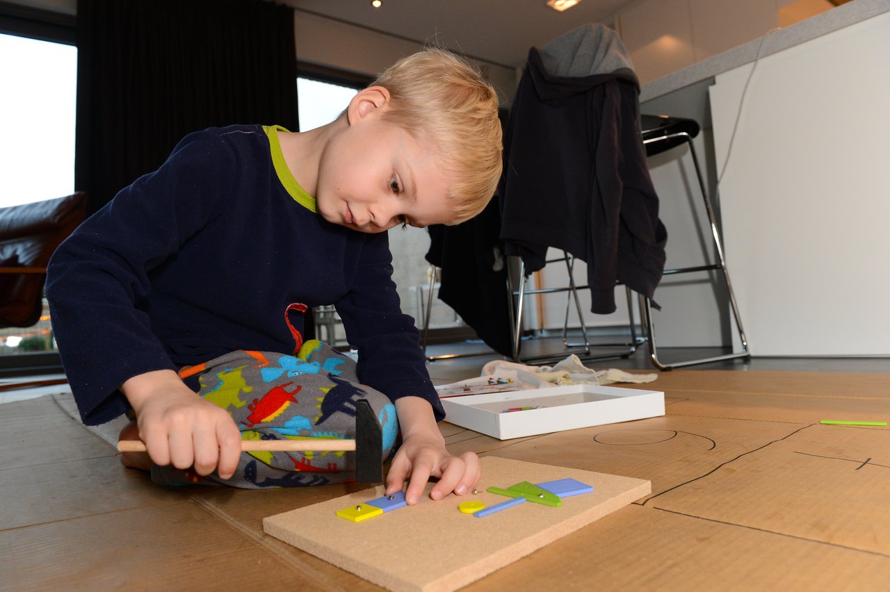 A young child hammers small colorful pieces onto a board while focusing on a craft project.