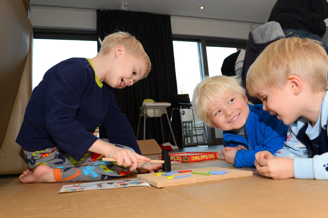 Three young children sit on the floor, playing a board game together and smiling.