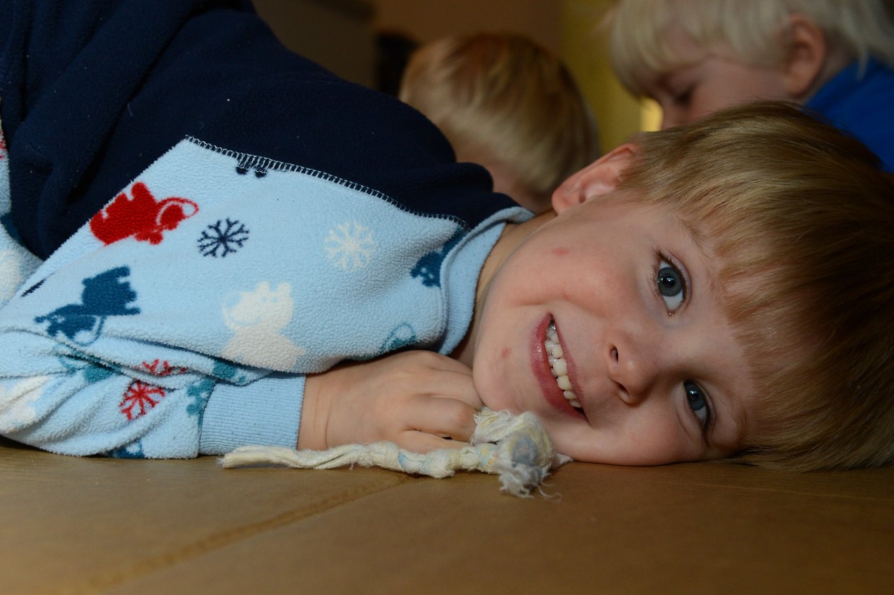 A smiling child in festive pajamas lies on the floor, looking at the camera.