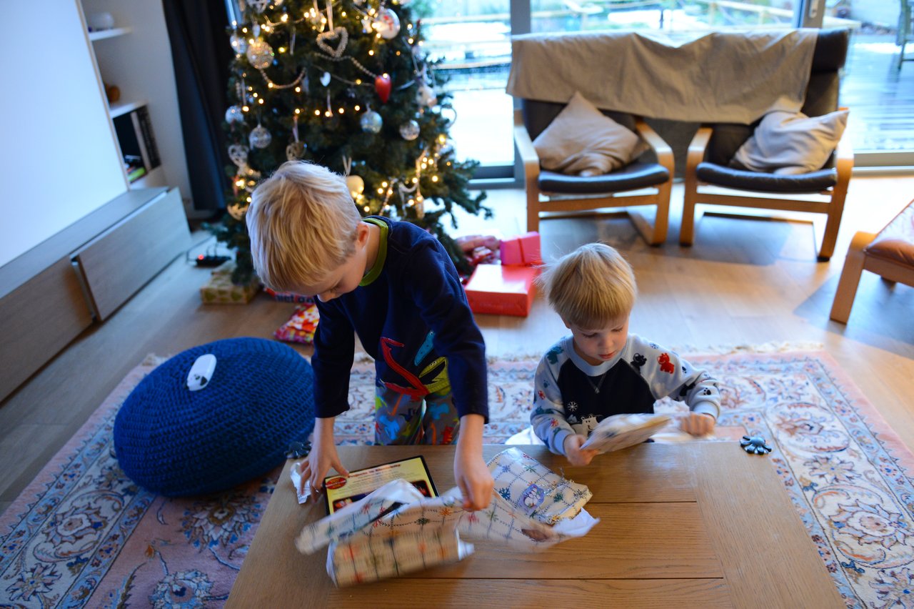 Two children excitedly unwrap gifts near a Christmas tree in a cozy living room.