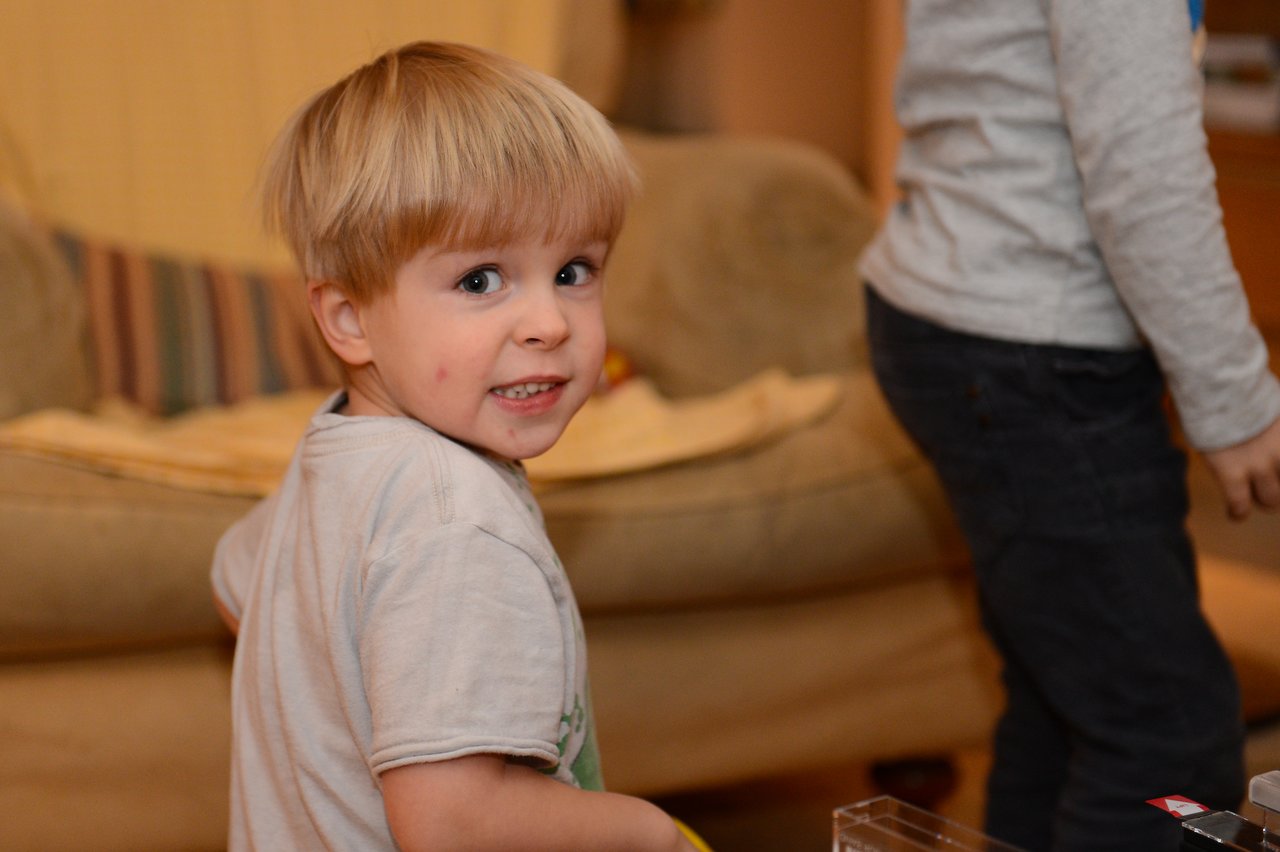 A young child in a white shirt looks back and smiles, while another child stands nearby.