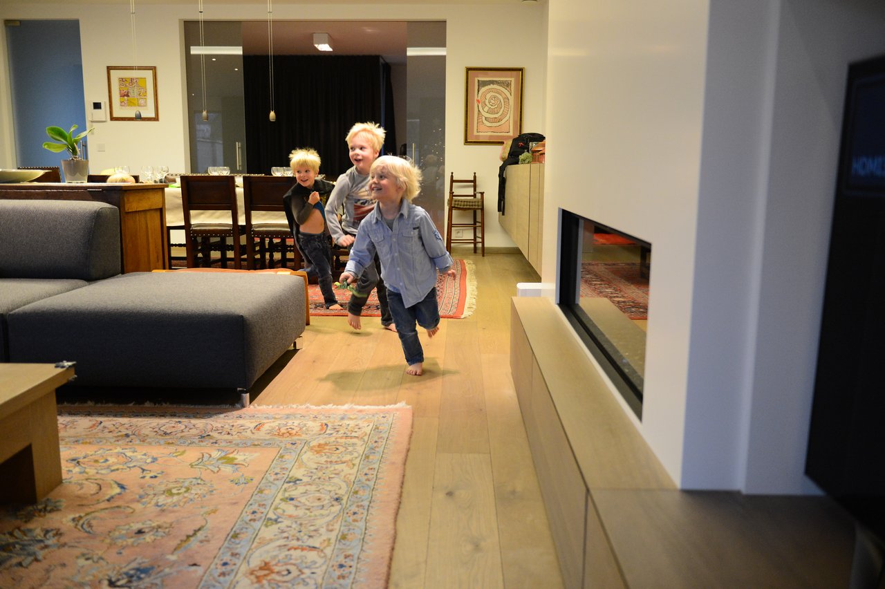 Three young children run barefoot through a warmly lit living room, smiling and playing together on Christmas Eve.