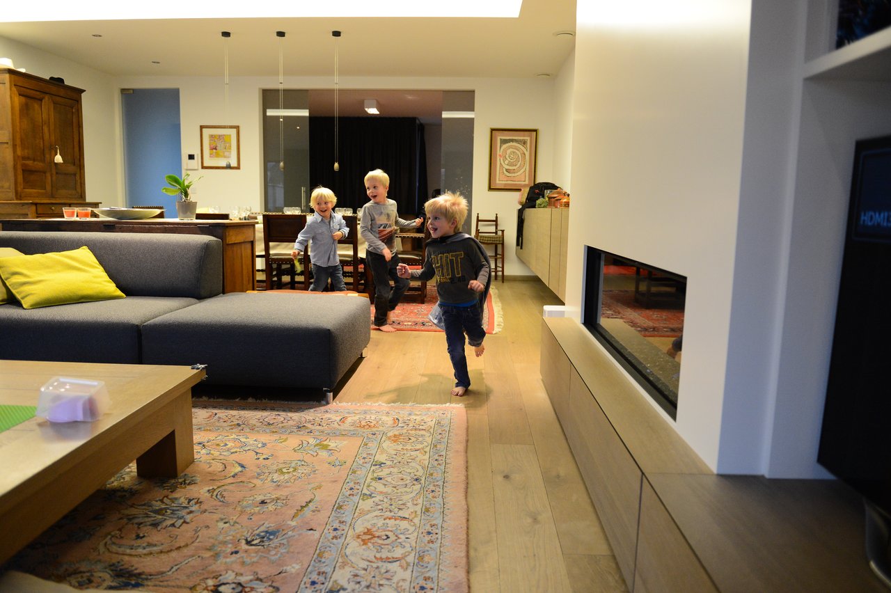 Three young children run and play in a warmly lit living room on Christmas Eve.