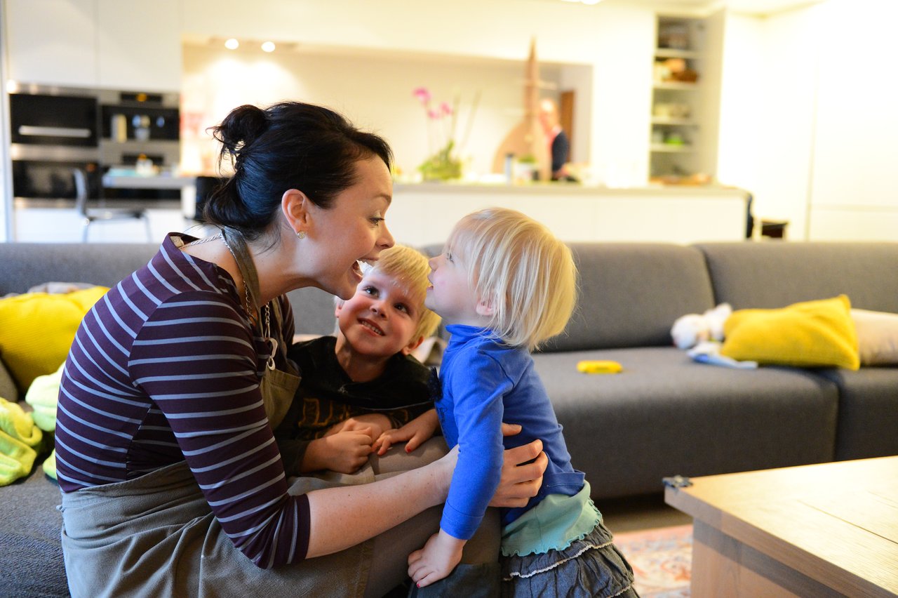 A woman and two children share a joyful moment in a cozy living room on Christmas Eve.