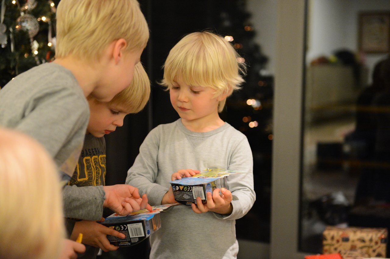 Three young children examine their new toys together near a Christmas tree on Christmas Eve.