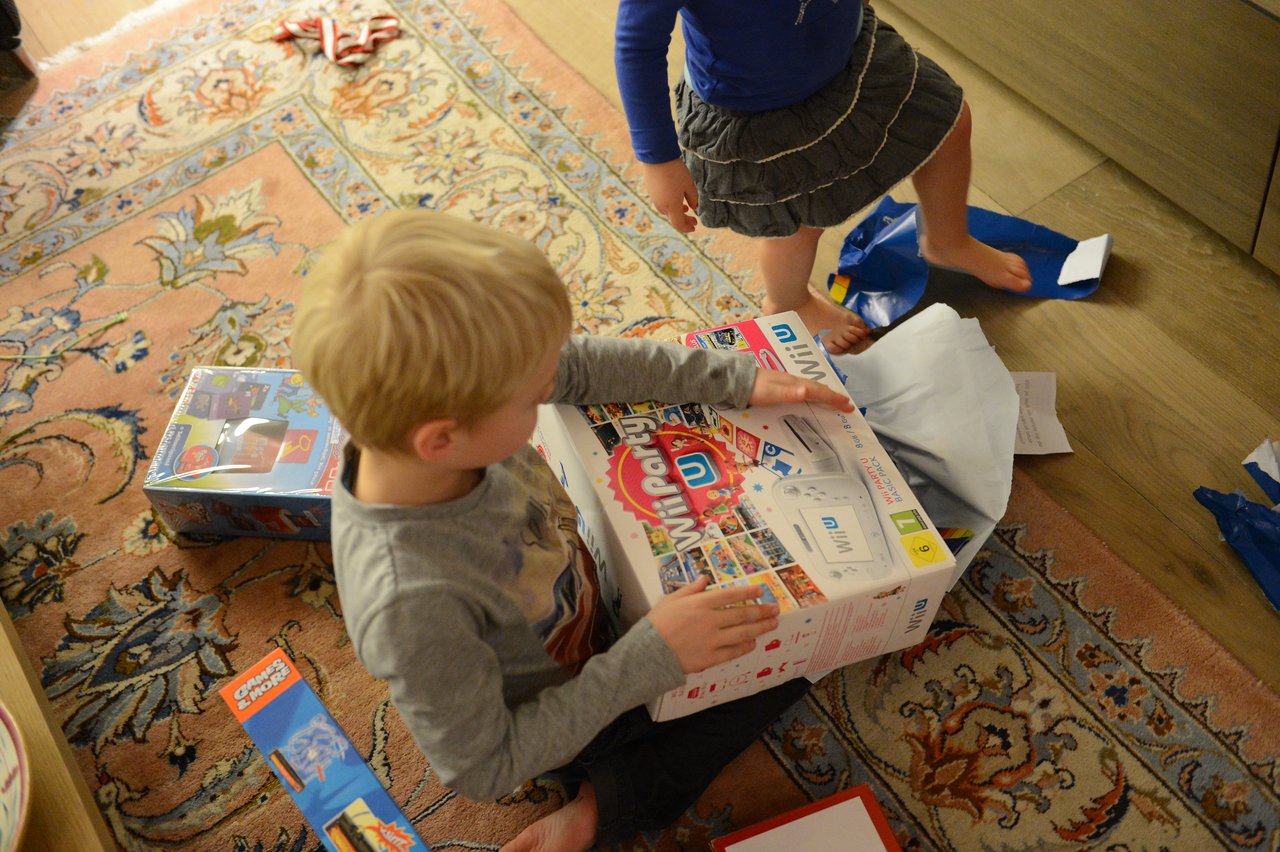 A child sits on the floor, excitedly holding a newly unwrapped Wii U console on Christmas Eve.