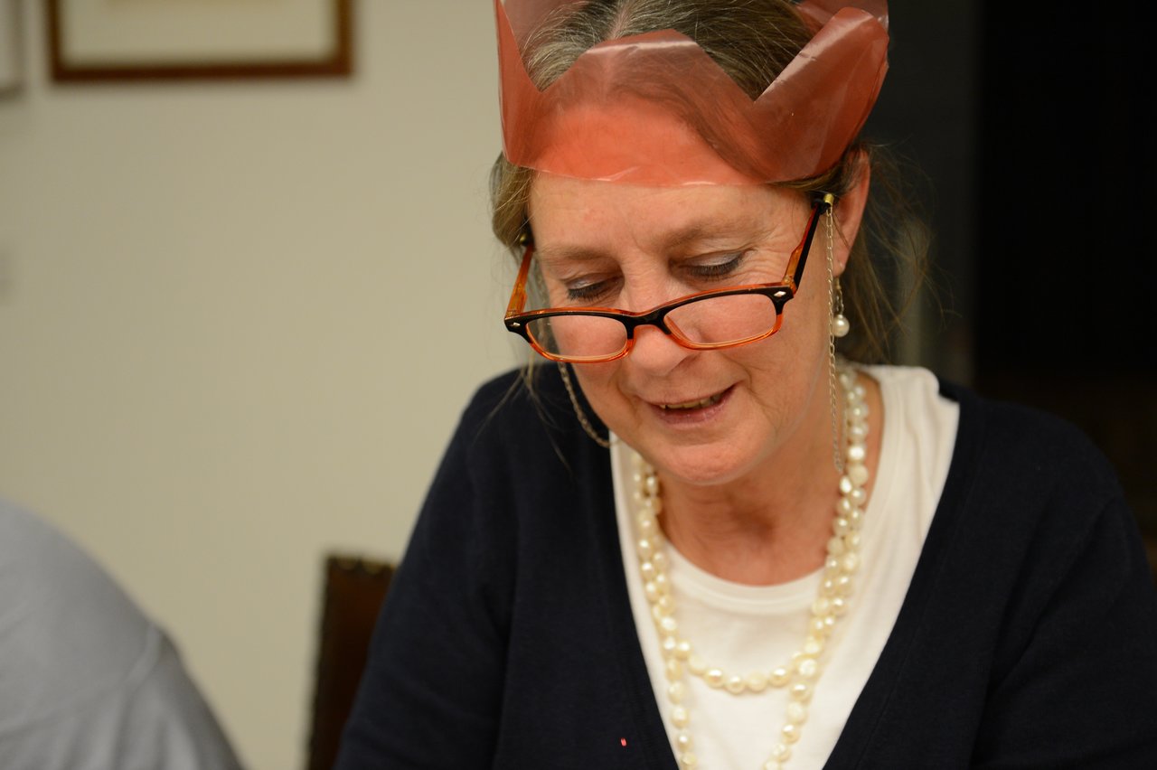 A woman wearing a paper crown and glasses looks down while engaged in an activity on Christmas Eve.