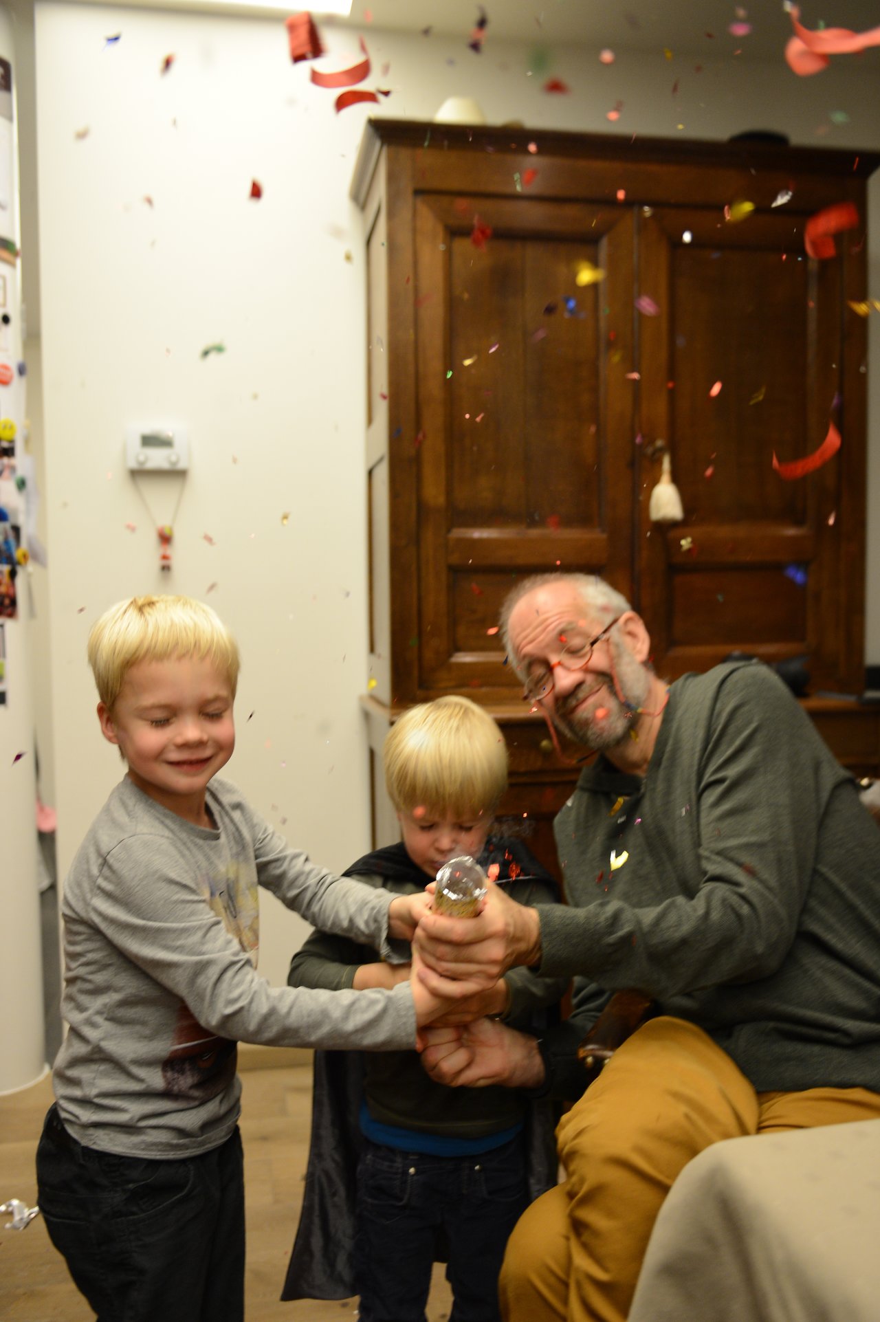 An older man and two children pop a party cracker, releasing confetti in a festive Christmas celebration.
