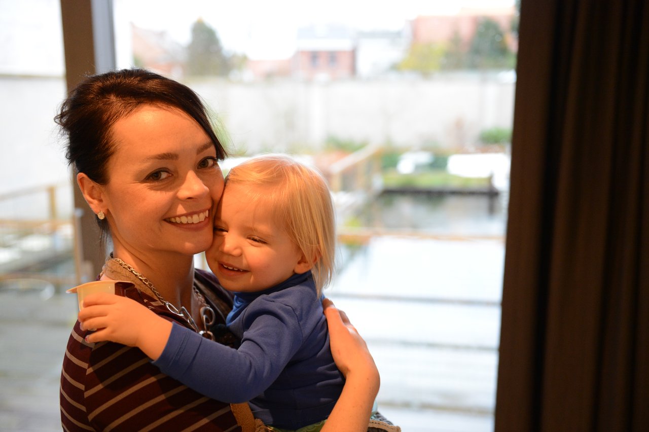 A smiling woman holds a young child in her arms indoors near a window on Christmas Eve.