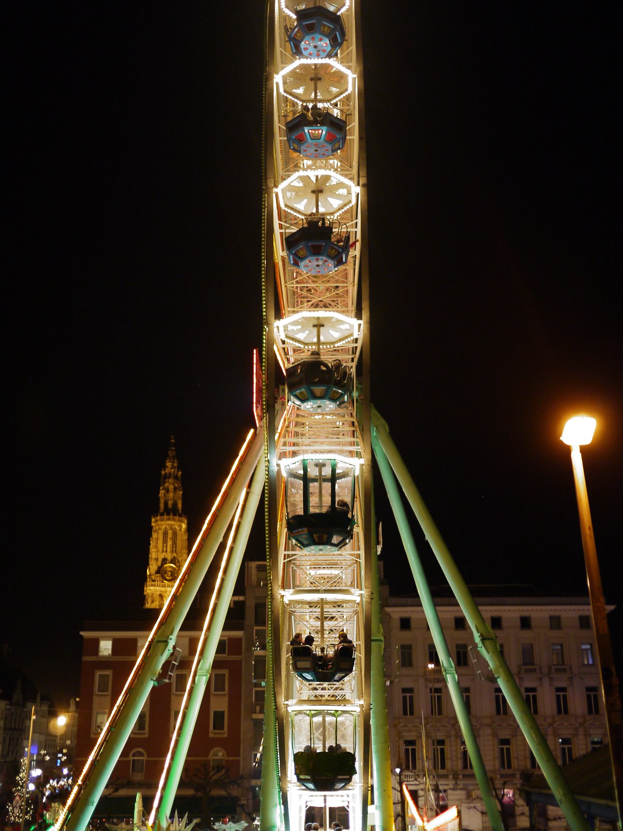 A large Ferris wheel with glowing lights stands at a Christmas market in Antwerp at night.