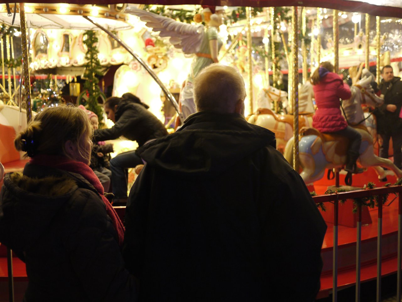 People watch children riding a brightly lit carousel at a Christmas market in Antwerp.