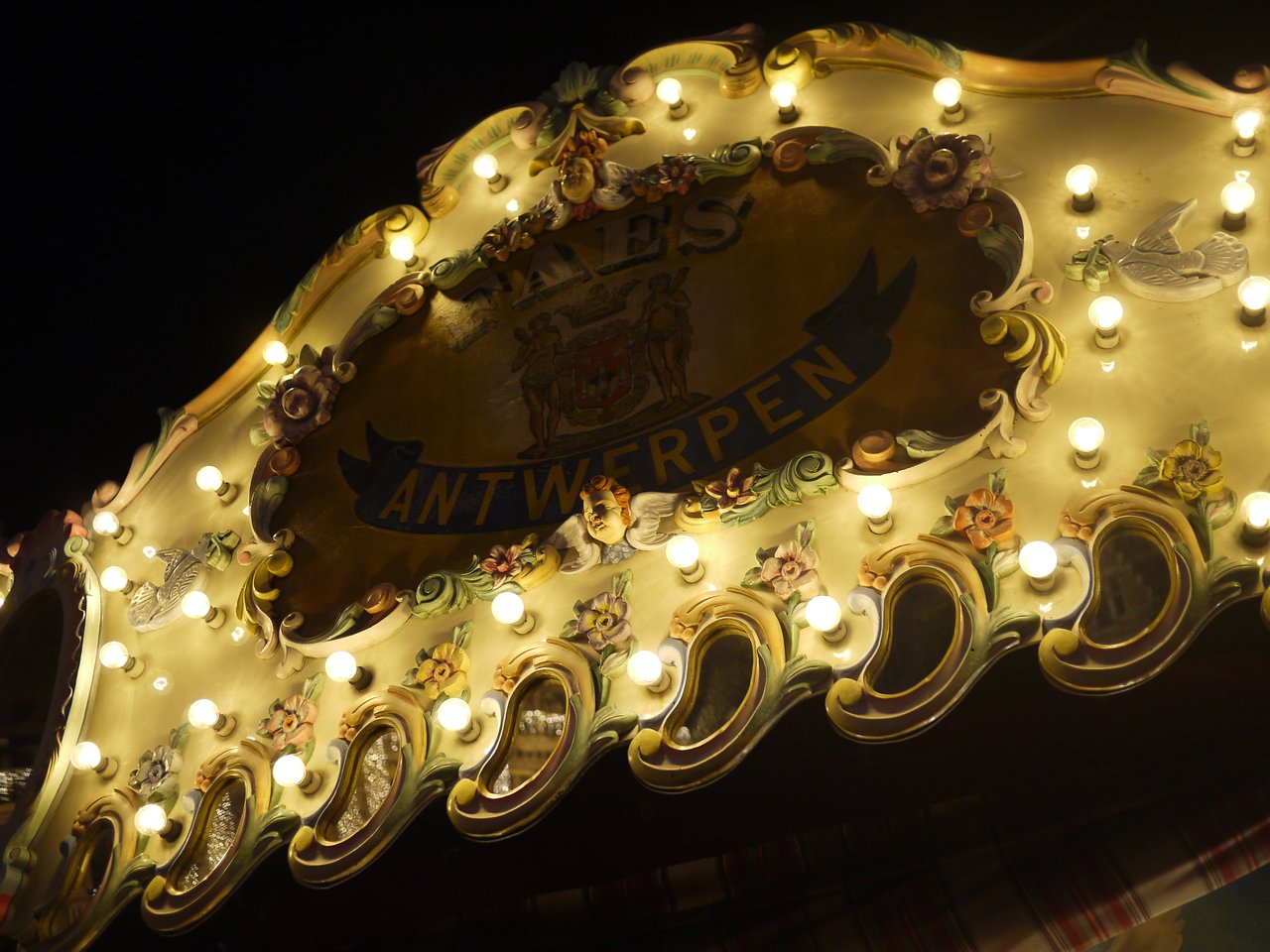 Illuminated decorative sign with "Antwerpen" at a Christmas market in Antwerp, featuring ornate details and glowing lights.