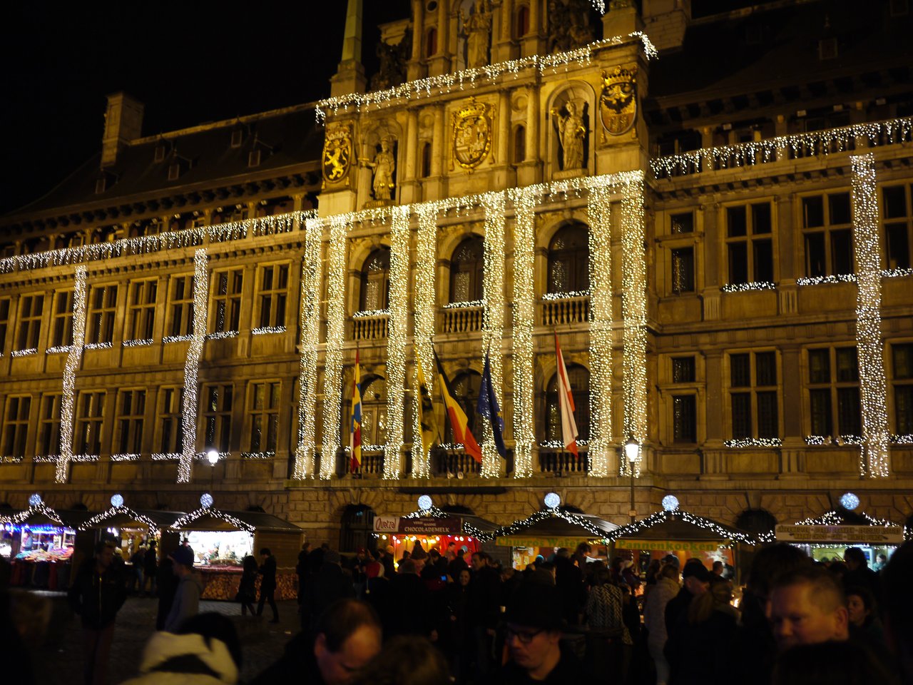 A Christmas market in Antwerp with festive lights, wooden stalls, and a crowd enjoying the holiday atmosphere at night.