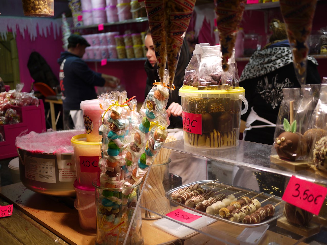 A Christmas market stall in Antwerp selling sweets, chocolates, and candy, with vendors preparing treats.