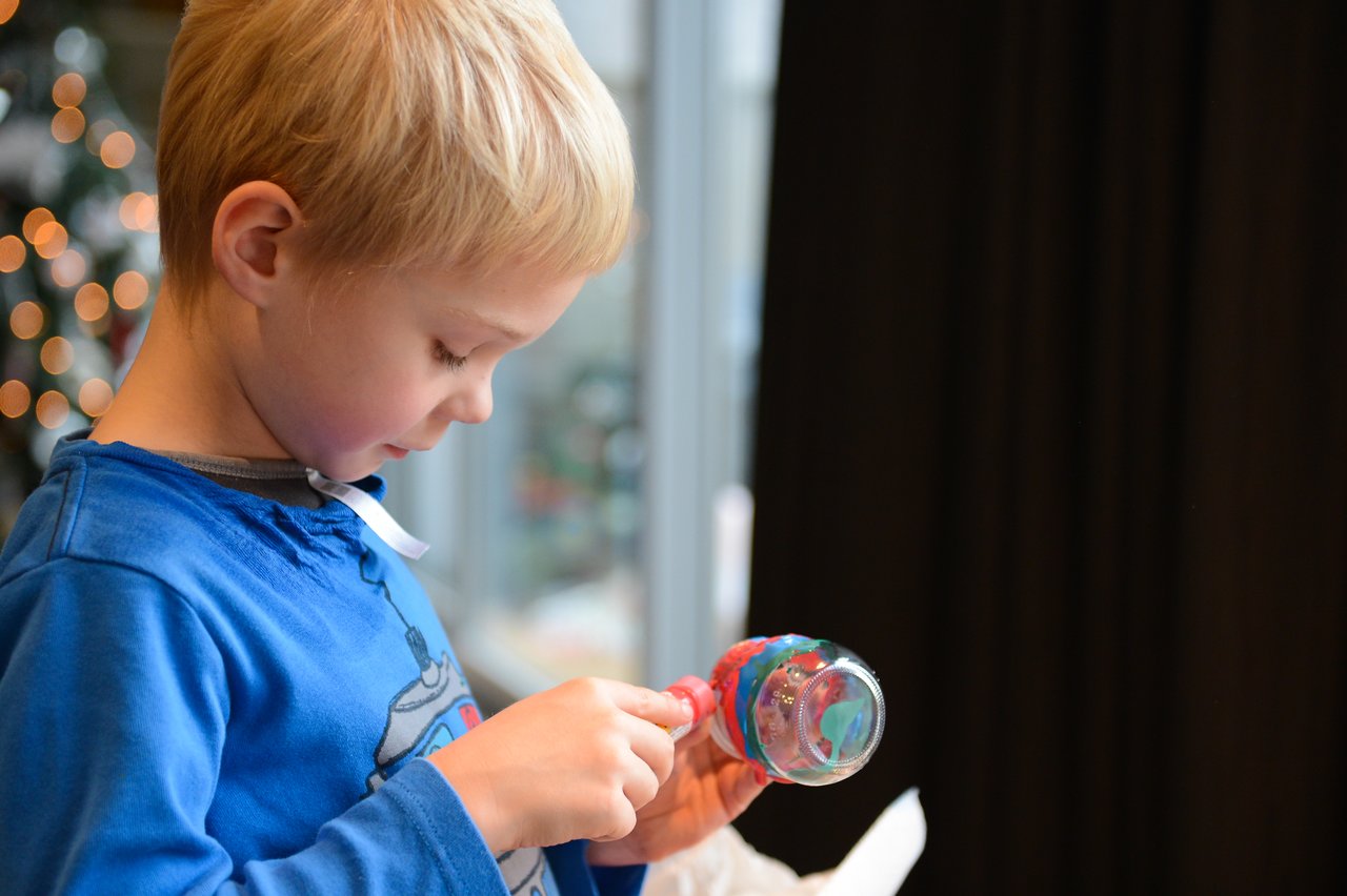 A child in a blue shirt carefully paints a small glass ornament with red and blue colors.