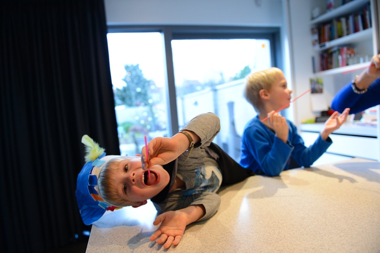 Children play a game using straws, with one child lying on the counter and reaching out playfully.