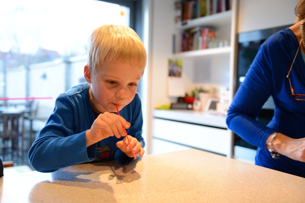 A child in a blue shirt uses a straw to play a game at a kitchen counter.
