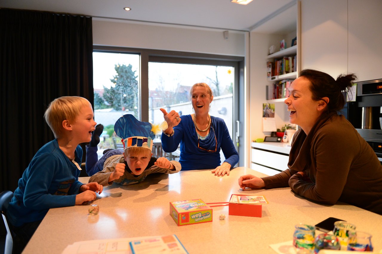 Two children and two adults laugh and play a board game together at a kitchen counter.