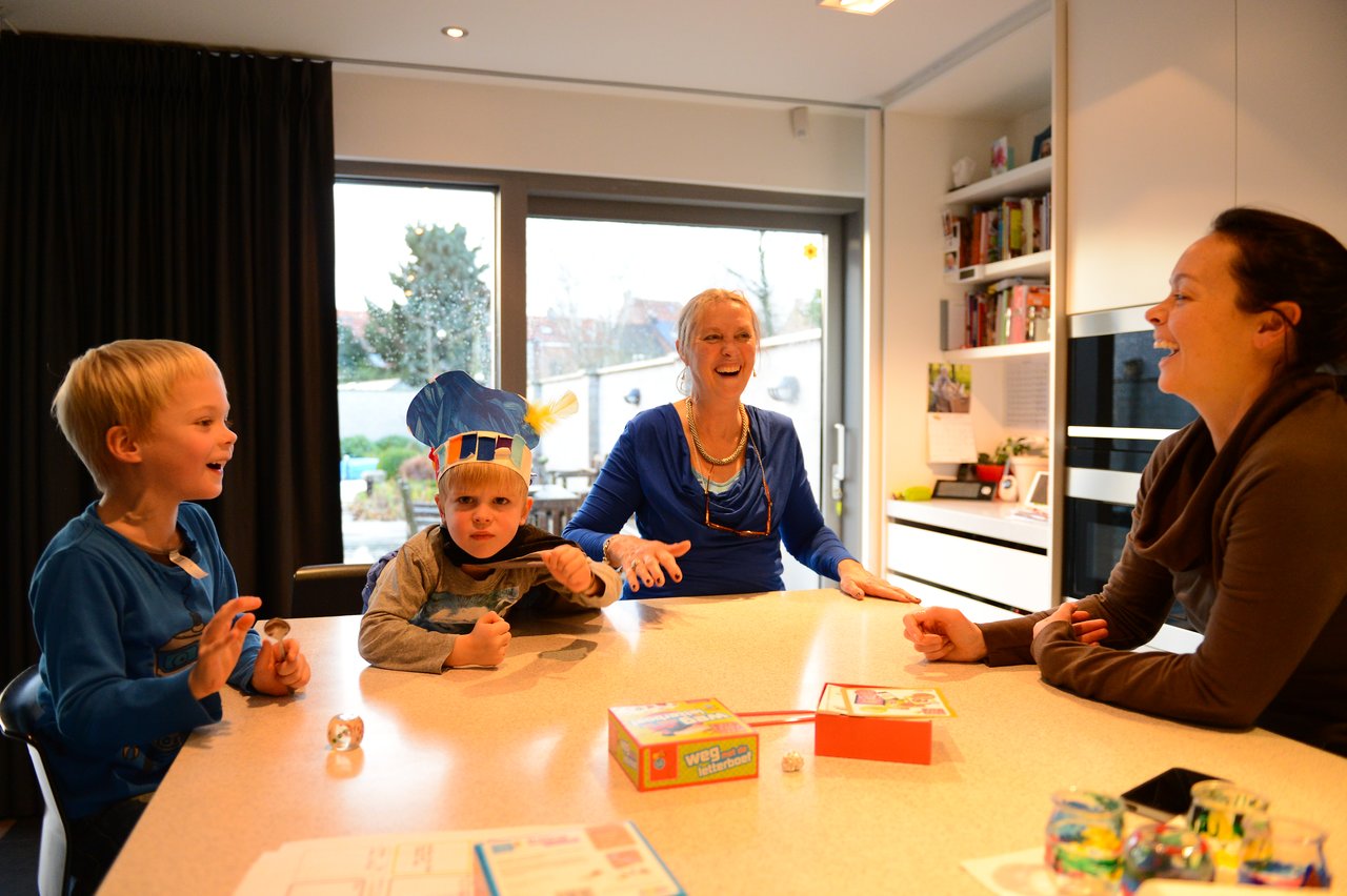 A family gathers around a table, playing a board game and laughing together in a bright kitchen.