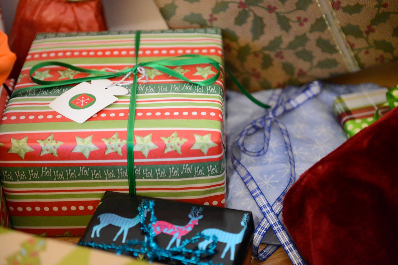 Several wrapped Christmas gifts with colorful ribbons and tags are placed together on a surface.