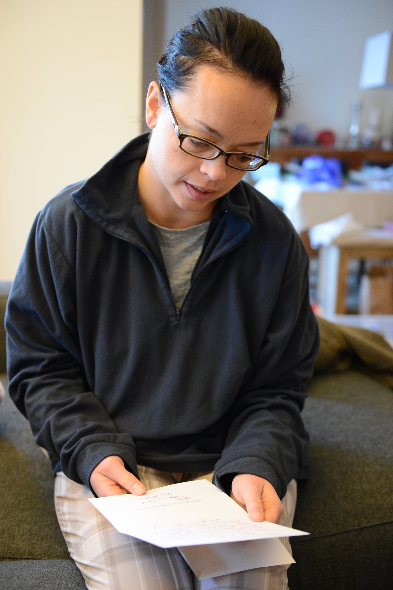 A person sits on a couch, reading a handwritten card while holding additional papers in their hands.