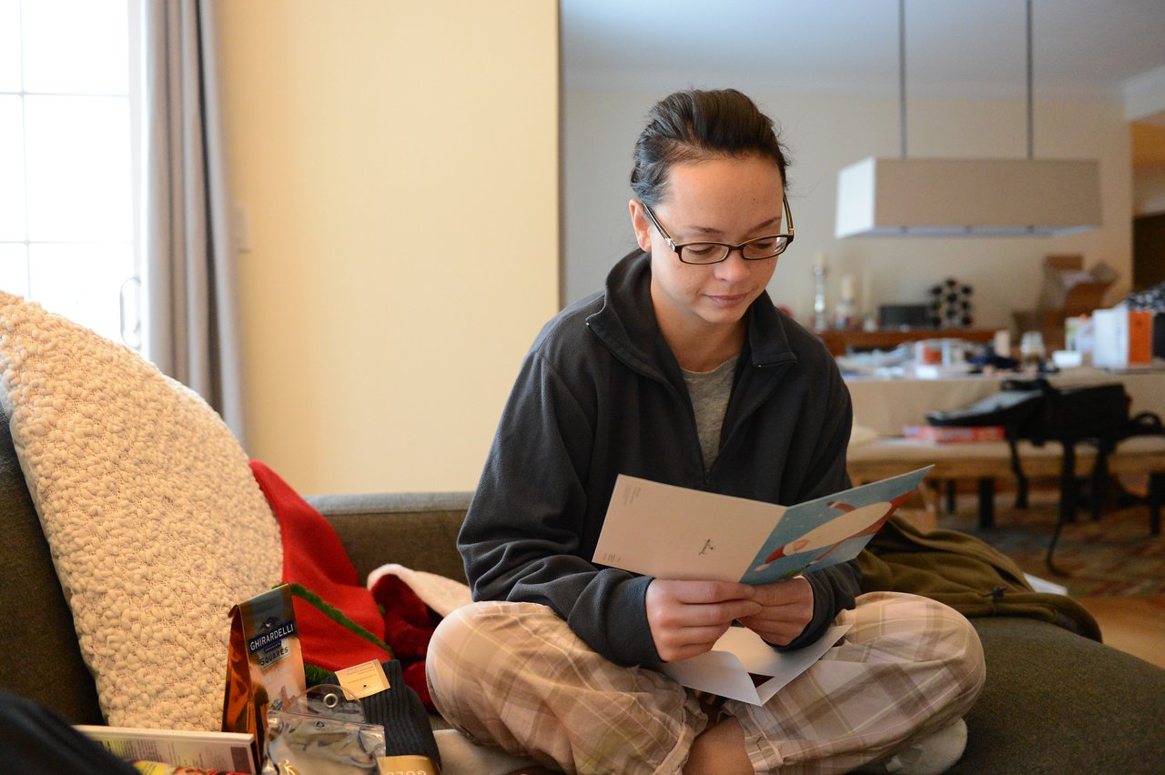 A person sits on a couch, reading a holiday card while surrounded by gifts and festive items.